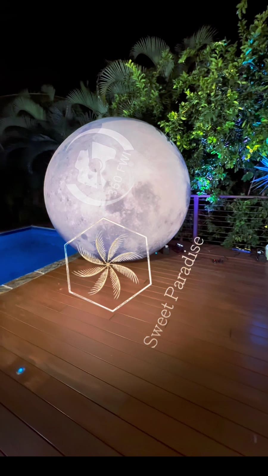 Une lune géante lumineuse posée sur le deck, au bord de la piscine, à la nuit tombée