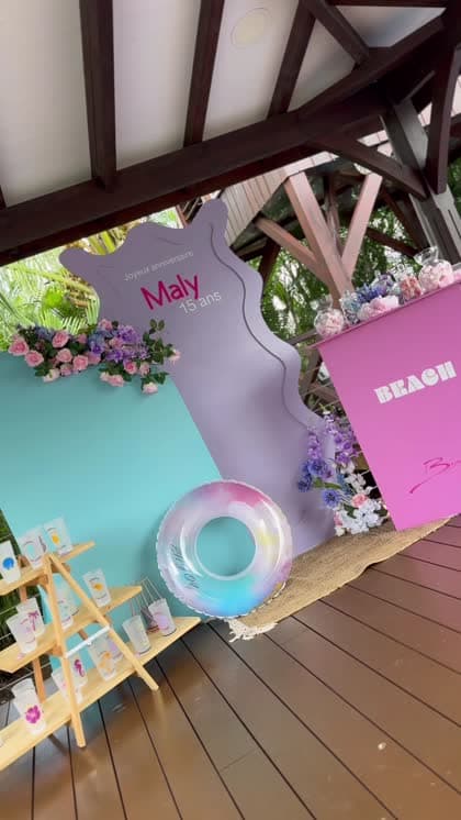 Le décor d'un anniversaire sur le thème de la plage : présentoir, gobelets personnalisés, tables roses et bouées dans la piscine