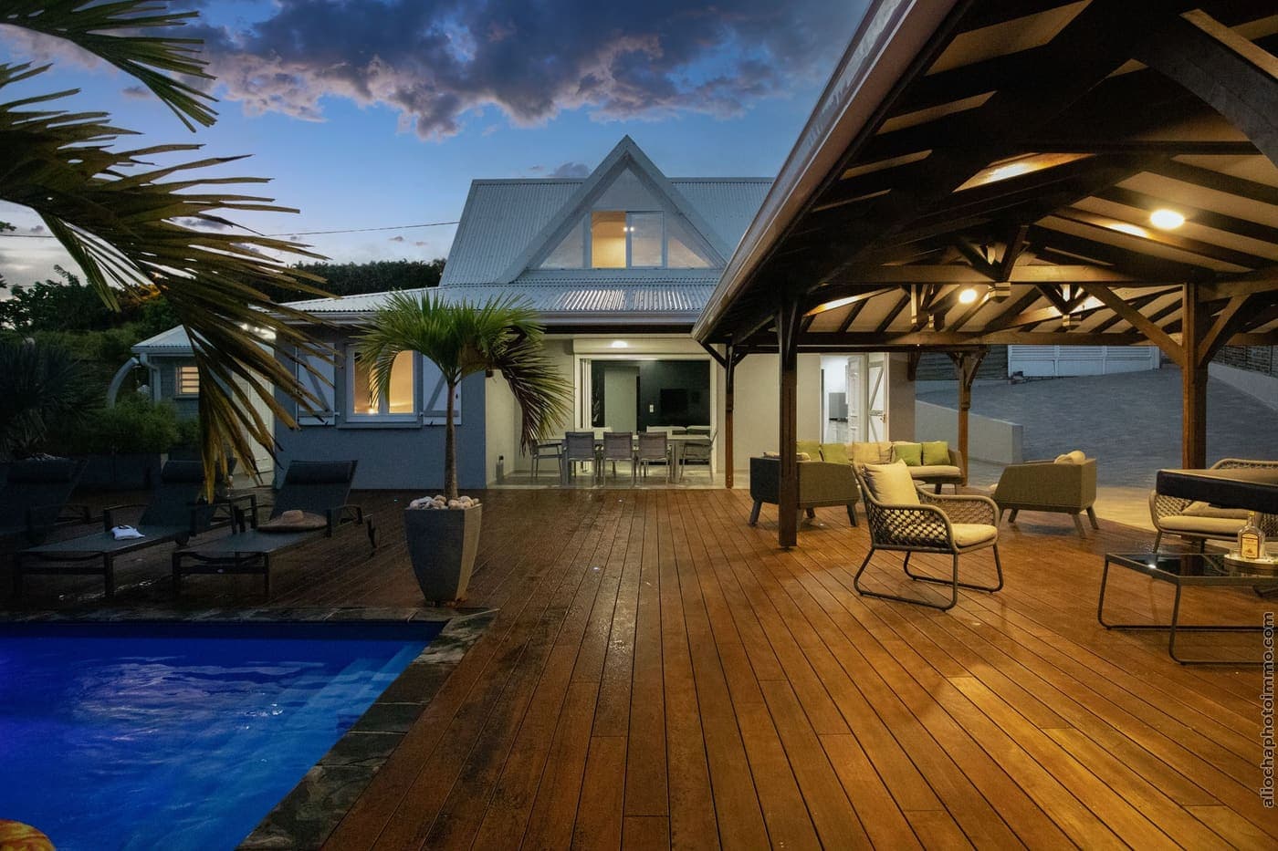 The ipe-wood deck and the pool lit up at nightfall, under the carbet