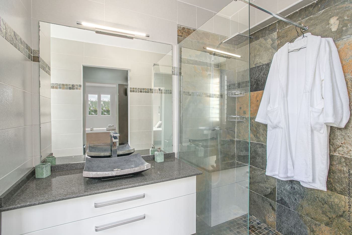 Une salle de bain de la villa : douche à l'italienne vitrée, vasque et peignoirs